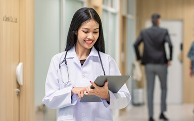 Portrait female beautiful Asian doctor wearing uniform, stethoscope, smiling with confidence, holding tablet, standing at hallway in hospital or clinic. Health care Concept.