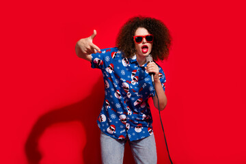 Photo portrait of lovely young lady hold mic singing cheeky cool rap wear trendy blue print x-mas garment isolated on red color background