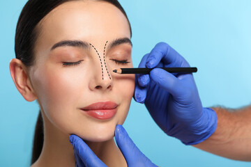 Woman preparing for cosmetic surgery, light blue background. Doctor drawing markings on her face, closeup