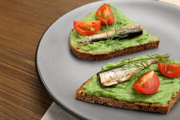 Delicious sandwiches with sprats, tomatoes, avocado puree and dill on wooden table, closeup. Space for text