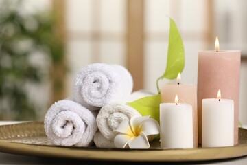 Fototapeta na wymiar Spa composition. Burning candles, plumeria flower, green leaves and towels on table indoors