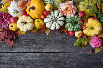 Wooden background with pumpkins, fruits, flowers, plants, leaves, apples, roses, decorative grapes, viburnum berries, rosehips. Autumn holiday card, Halloween, Thanksgiving, place for text.