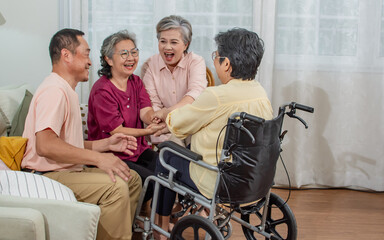 Fototapeta na wymiar Group senior Asian aging warm female sitting on sofa in cozy nursing home, encourage friend who sitting on wheelchair, smiling with happiness. Retirement, Healthcare, Aging Society Concept.