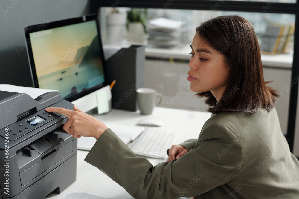 Poster young confident businesswoman pressing button on panel of xerox machine while setting number of copi