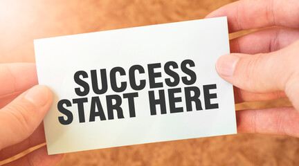 SUCCESS START HERE word inscription on white card paper sheet in hands of a businessman.