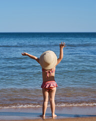Little girl looking at the sea with arms up on a sunny day