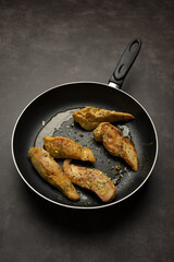 Fried pieces of meat in a frying pan on a dark background. Fried steaks in a frying pan. Top view, vertical position, close-up