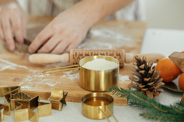 Man making christmas gingerbread cookies close up in modern white kitchen. Hands cutting gingerbread dough with festive golden metal cutters with cooking spices and decorations