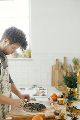 Man making christmas gingerbread cookies close up in modern white kitchen. Hands cutting gingerbread dough with festive metal cutters with cooking spices and decorations