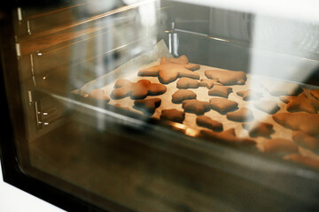 Gingerbread cookies in christmas festive shapes on tray baking in oven in modern white kitchen. Making christmas gingerbread cookies