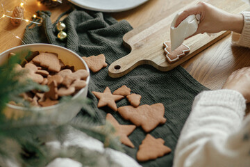 Hands decorating christmas gingerbread cookies with icing on rustic wooden table top view....
