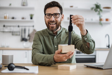 Caucasian male influencer wearing eyeglasses recording video blog about unboxing of new smart watch. Bearded young guy doing review of modern gadget while working from home.