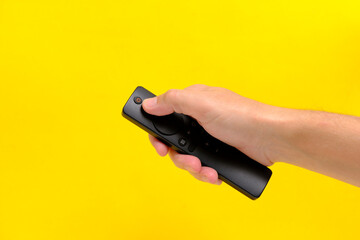 Hand yellow background holds TV remote by pressing button with finger.
