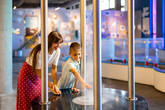 Mom with a little boy learn physics interactively on a model that shows physical phenomena while visiting a science museum. Concept of children's entertainment and learning
