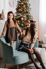 A young mother and her happy daughter are having fun against the backdrop of a beautifully decorated New Year tree. Mom and daughter have fun while enjoying the Christmas holidays