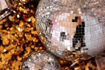 Bright silver glowing mirror disco balls on gold confetti background. Trendy New year 2024 party,...