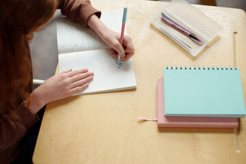 Above angle of hands of secondary school learner drawing in copybook with pen while sitting by desk...