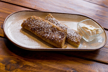 Pancakes with sour cream sprinkled with sugar on a plate on a wooden table