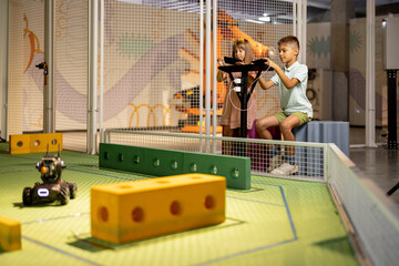 Kids playing with robotic cars controlling them with remote controls on a playground in science...