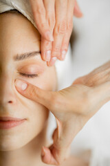 Adult woman receiving relaxing facial massage, close-up top view on woman's face during a massage. Massaging the area under eyes