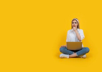 Blonde girl pondering over a problem, full body view caucasian blonde girl pondering over a problem. Sit floor legs crossed hold laptop touching chin  with hand looking aside copy space. Pensive.