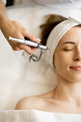 Young woman receiving oxygen mesotherapy on her face, close-up view from above. Concept of...