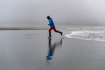 A sportsman is jogging on the ocean beach and running from the waves while exercising in nature.