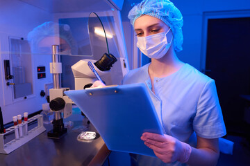 Female scientist taking notes after microscopic examination of cell samples