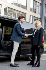 Female chauffeur greets the businessman while helping him to get out of the minivan taxi. Concept of personal driver, luxury taxi for business people