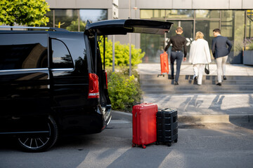 Driver or concierge helps a business couple carry their suitcases to the office or hotel from a minivan taxi. Concept of business travel and transportation service - obrazy, fototapety, plakaty