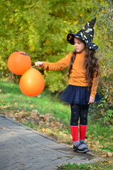 happy laughing child girl in witch costume to halloween. with a jack-o'-lantern candy bowl, trick or treat, in a witch's hat, with colorful balls in the autumn forest, eating spider-shaped candy