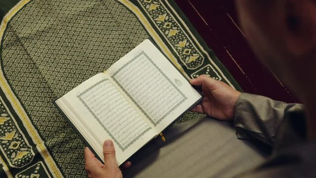 Muslim man reading The Quran holy book on a prayer mat. TRANSLATION of the muslim prayer: "God is the greatest"