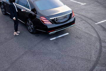 Female chauffeur near premium car on parking lot, view from above. Business transportation and...