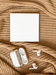 On a beige knitted background there is a white square with a place for text, next to white wireless new headphones