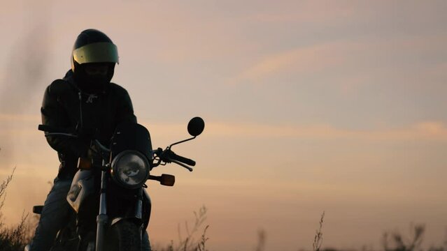 motorcyclist in a helmet and leather jacket at sunset with a classic motorcycle. Motorcycle life concept