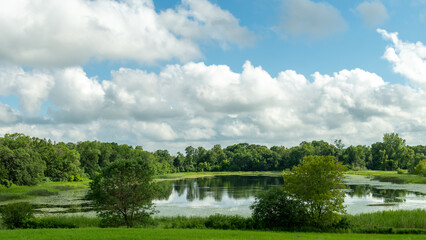Fototapeta na wymiar Panoramic view of a body of water with trees and blue skies in the summer in rural Minnesota, USA. 
