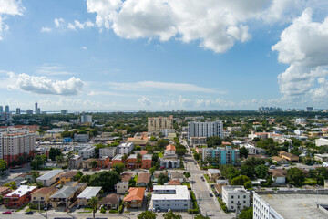 stunning aerial view with hotels, office buildings and skyscrapers in the city skyline, homes and apartments surrounded by lush green trees, cars on the street, blue sky and clouds in Miami Florida