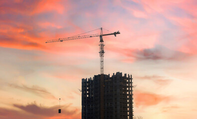 Silhouettes of tower cranes constructing a new residential building at a construction site against...