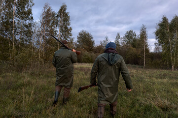Fototapeta na wymiar Hunters on hunt. A hunter walks through forest among trees in search of wild birds or wild animals. Hunters with gun and rifle on hunting in fall season. Hunter during hunting on elk in forest.
