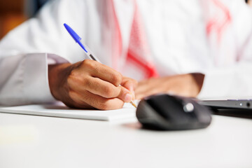 Middle Eastern freelancer efficiently works at his desk, scribbling in his notebook. He conducts...