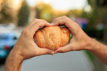 Guy's hand holds a croissant, close-up concept of snack and fast food. Selective focus on hands with blurred background