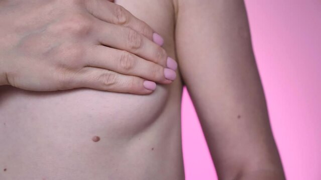 Woman with small breasts, size AA, doing breast self-massage and checking for breast cancer, close-up, pink lighting. Caring for yourself and your health at a mammologist. Female part body isolated