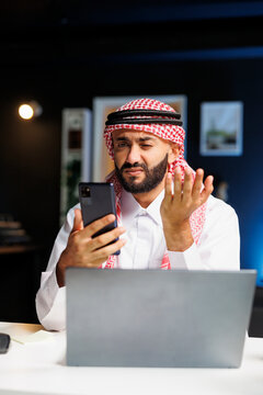 Arab guy engrossed in a video conference call with a coworker on his smartphone. He expertly uses wireless technology for work and research, showcasing his digital communication skills.