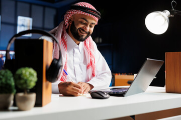 A focused guy entrepreneur in business attire sits at a desk using his laptop. Arab man uses his...