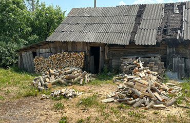 Pile of chopped firewood in village near house. Chopping wood and cutting timber. Preparation of firewood in village for heating house in winter. Old barn in countryside. Rural landscape.