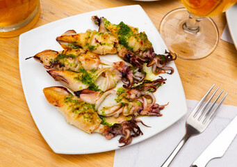 Service plate containing roasted calamari with pesto sauce with necessary table laying