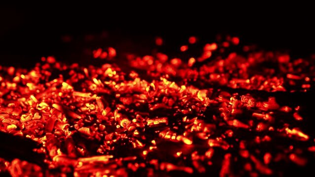 Smoldering red embers scattered on the ground. Smoke goes up and charcoal flashing from the wind. Close up.