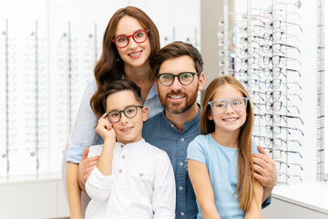 Portrait of young smiling family hugging choosing stylish glasses in modern optical store. Vision...