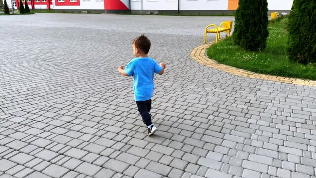 Following a beautiful toddler running outdoors. Smiling active Caucasian kid having fun on the walk in summer.