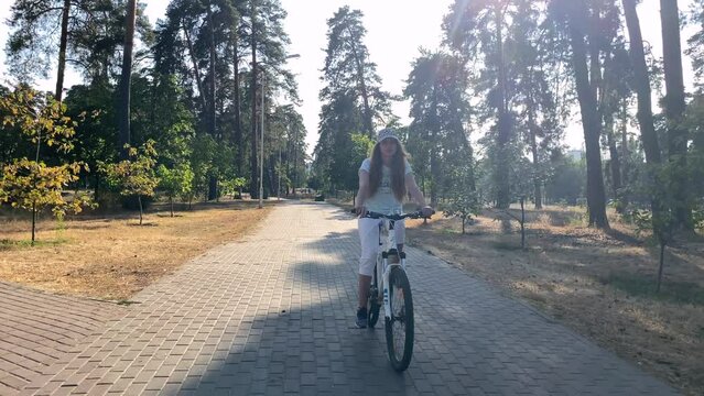Fitness training on a bicycle. A girl on a bicycle on a beautiful summer day. Bike rides in the fresh air. A woman rides a bicycle on a park path. High quality 4k video